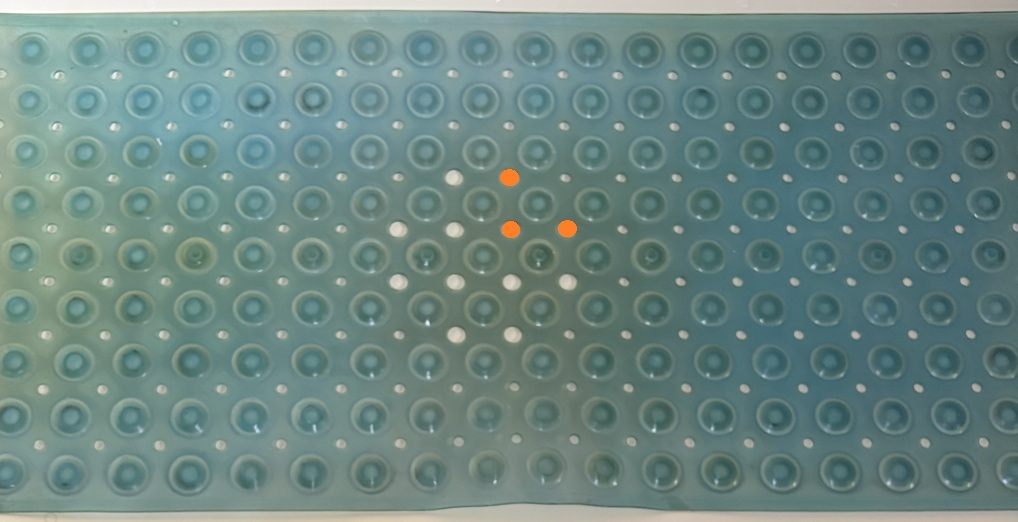 Old blue bath mat with many white holes and a cross of larger white holes.