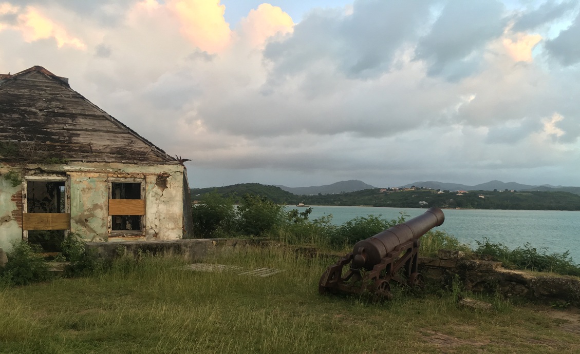 Iron cannon aiming out to sea beside a run down building
